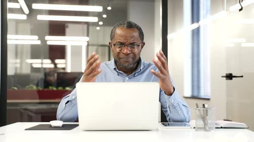 Upset worried african american businessman reads bad news on laptop sitting at desk at workplace