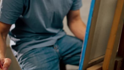 Close Up Young Artist in a Blue Tshirt in an Art Studio Working on Painting While Sitting