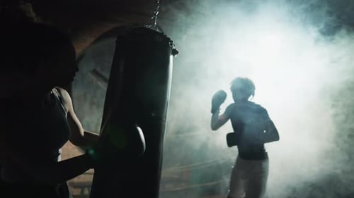 Silhouette of Athletic Male Boxer Fighter Training with Punching Bag in Gym Cinematic Shot in