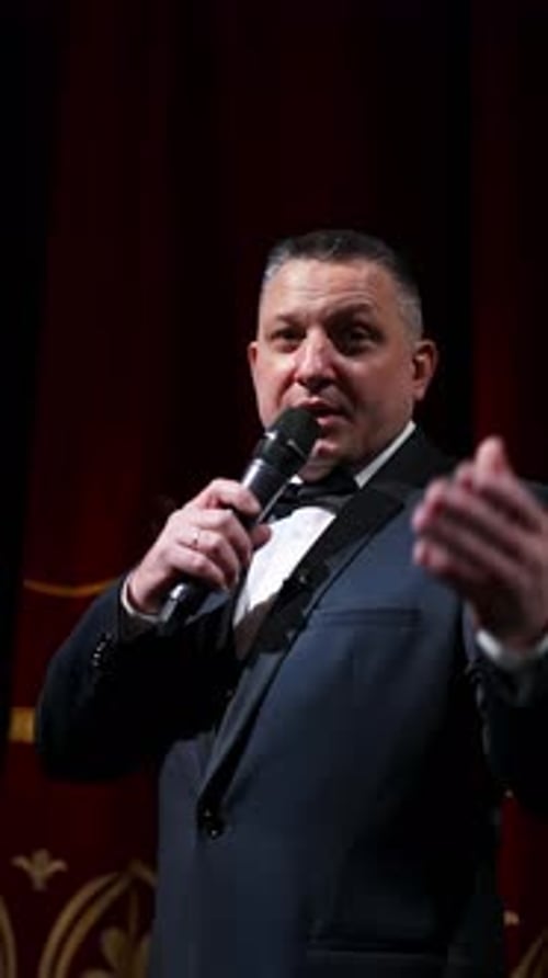Actor with microphone announces performance before auditorium. Theater curtains background.