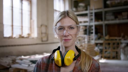 Confident female carpenter in workshop looks at camera small business concept