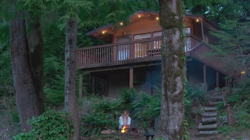 Young Woman Sitting at the Fire Pit Outdoor Cozy Wooden Cabin Hidden in Forest