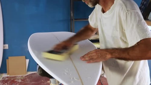 Man Shaping Surfboard with Sanding Block in Workshop