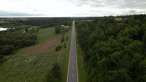 Aerial shot of the long highway with driving cars surrounded by green lush trees from both sides