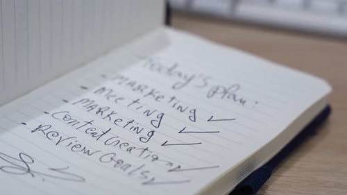 Handgeschriebene Checkliste für den heutigen Plan in einem offenen Notizbuch auf einem Holzschreibtisch