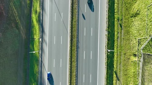 Top‑down aerial view of two parallel highway lanes with moving cars and grassy edges in bright