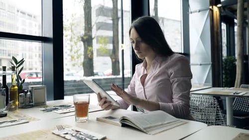 Young student studying at a cafe table with her tablet and textbook