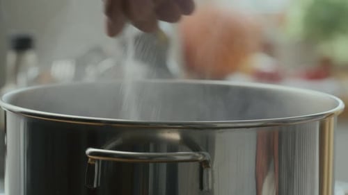 Hand Sprinkling Salt into Steaming Steel Pot during Cooking