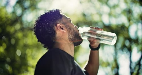 Athletic Young Man Drinks Water Outdoors in Sunlight