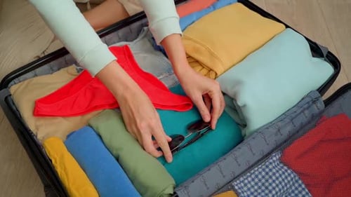 View of female traveler packing red panties and glasses in open suitcase