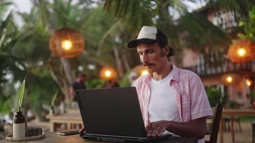Homem focado trabalha em laptop em café de praia durante o pôr do sol Trabalhador remoto conclui projeto perto do oceano