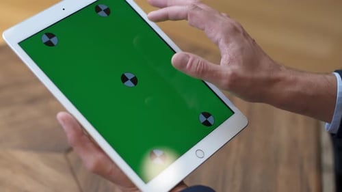 Ein Mann arbeitet an einem Tablet. Eine Hand in einem Anzug bewegt sich auf dem grünen Bildschirm. Nahaufnahme