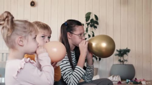 Children and Teen Blowing up Balloons Indoors