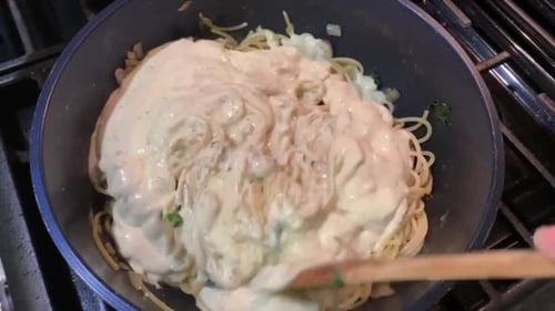 Cooking pasta with a white and creamy Alfredo sauce. Overhead cooking view.