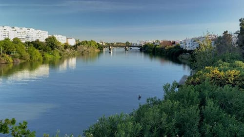 Rio Guadalquivir refletindo edifícios da cidade, árvores e pessoas curtindo a beira do rio em Sevilha