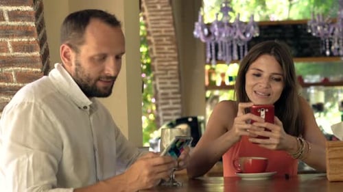 Couple Using Smartphones Sitting By Counter In Cafe
