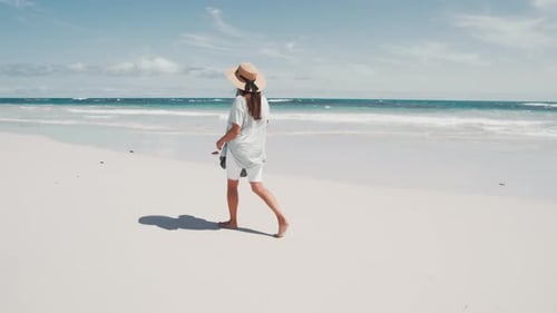 Woman walks barefoot on a sunny beach