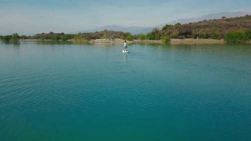 Aerial drone flying over a man doing stand up paddle in a blue water lake with mountains