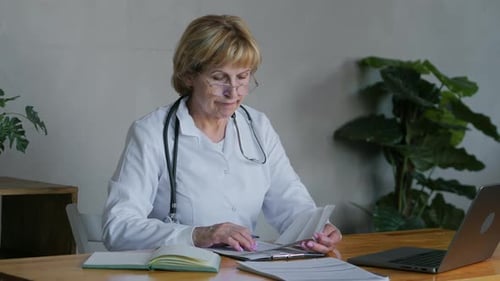 an Adult Blonde Female Medic Who is Working Intently at a Desk in the Office