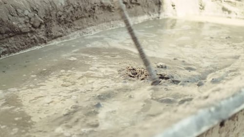 A construction worker mixes concrete in a container using an electric construction mixer. Close-up.