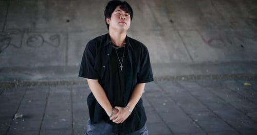 A stylish young man performs a freestyle dance under a footbridge in the city.