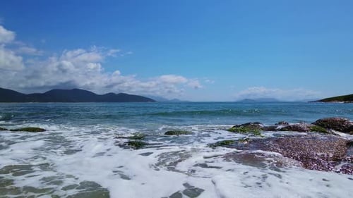 Close-up Footage of Beach Waves Coming Toward's some Small Mossy Rocks. No Camera Movement.