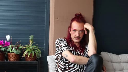 Non-binary person with red hair and mustache posing on balcony