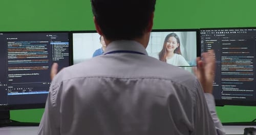 Nahaufnahme eines Entwicklers in der Rückansicht, der Video hat, während er Code mit mehreren Bildschirmen auf grünem Bildschirm schreibt