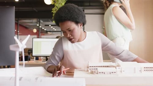 Happy african american female architect inspecting architectural model at work, in slow motion