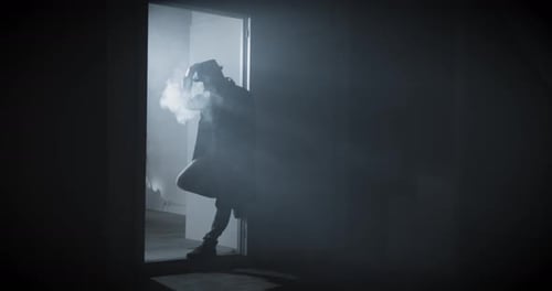 Noir Film Detective Standing in the Dark and Smoking a Cigarette Wearing Trench Coat