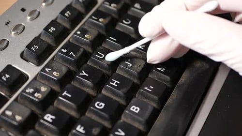 Close up clip of a man with a glove cleaning keyboard at office / home to disinfect the keyboard and