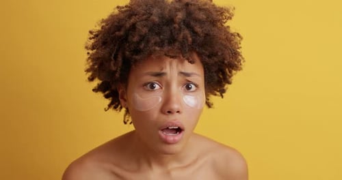 Une jeune femme ethnique stressée comprime les boutons sur le visage et applique des patchs de beauté inquiets