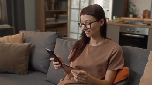 Woman using smartphone with credit card on sofa