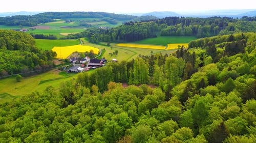 A Farm Stands on a Hill with Crop Fields White Bales of Hay and Pastures Surrounded By Forest