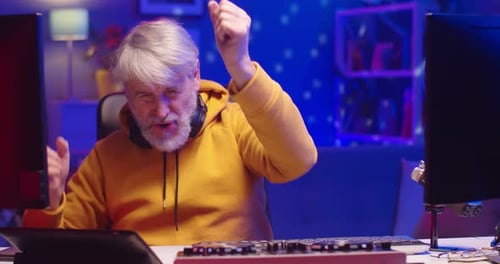 Close Up Portrait of Positive Joyful Caucasian Old Man DJ Sitting at Desk in Room in Neon Light