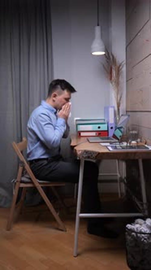Vertical Video Man Working From His Home Office While Unwell Blowing His Nose with a Tissue at His