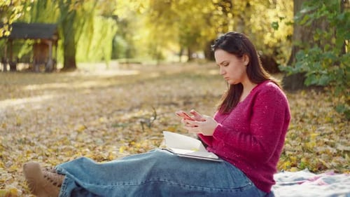 Woman Using Phone in Park with Dog in Autumn