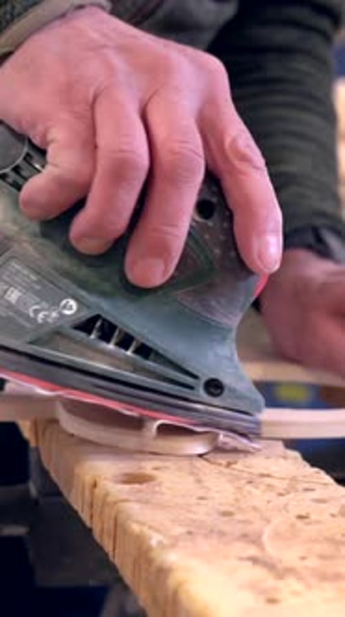 Concentrated carpenter polishing a piece of wood using electric tool in a workshop