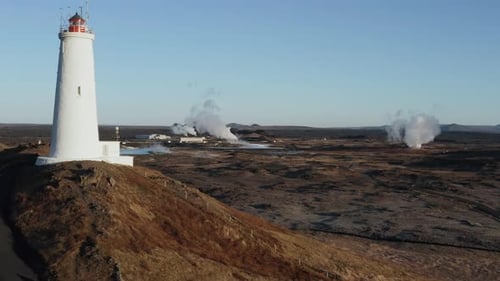 Iceland landscape with remote lighthouse and geothermal gas rising from field