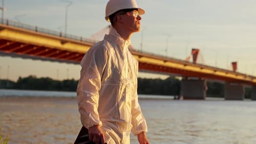 Environmental Inspector Surveying Riverbank Near Bridge