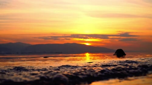 A sunset over the ocean with a rock in the water