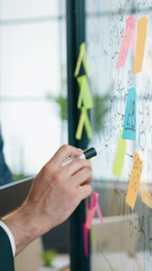 Man Writing on Glass Wall in Office Setting
