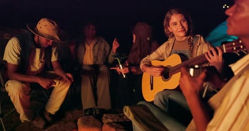 Friends Around Campfire at Night Playing Guitar