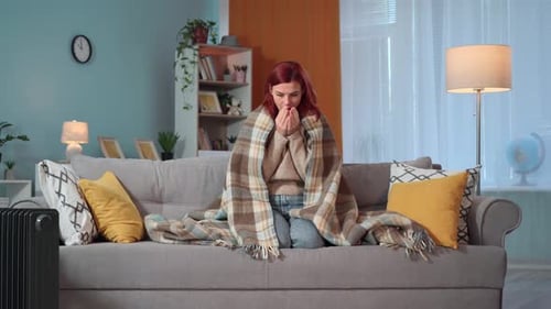 Portrait d'une jeune femme enveloppée dans une couverture chaude essayant de rester au chaud à cause du froid à la maison