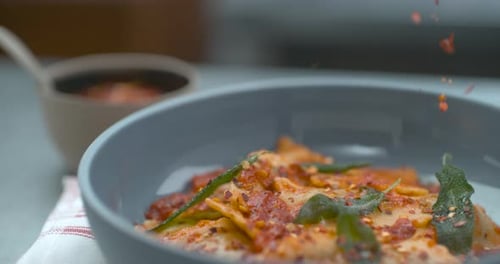 Chili Flakes Being Dropped Onto Tomato Ravioli Dish in Bowl in Ultra