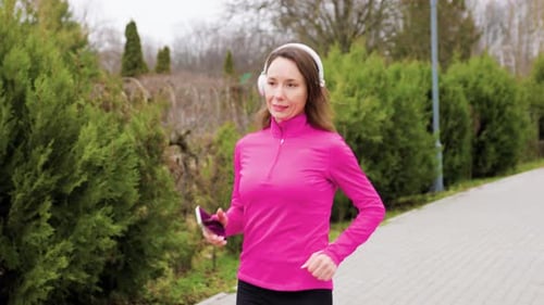 A Pretty Brunette Runner Going for a Jog in the Park Wearing Sportswear and Listening to Music