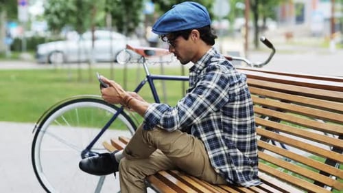 Man Using Phone on Bench with Bicycle Beside Him