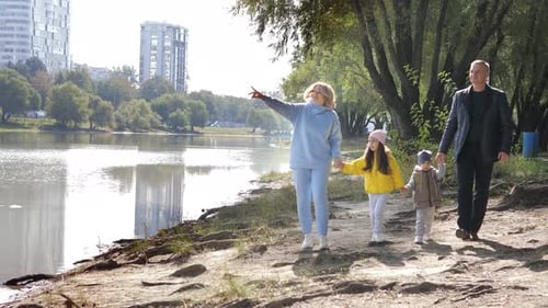 Young Couple of Grandparents with Two Little Grandkids Walking Along River Shore Holding Hands in