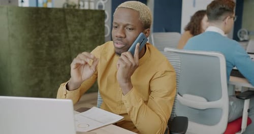 African American Businessman Speaking on Mobile Phone and Using Laptop in Shared Office