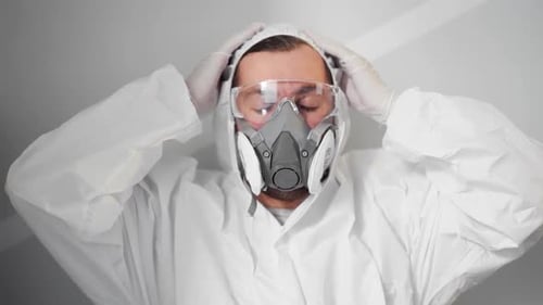 Close-up front view of doctor sitting on floor removes protective mask and respirator